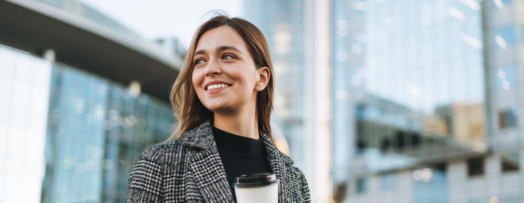 a woman holding a coffee cup and phone in the city